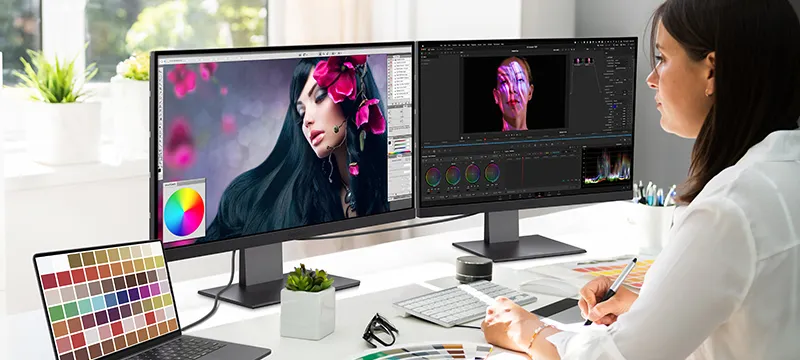 a woman uses graphic design software on two monitors