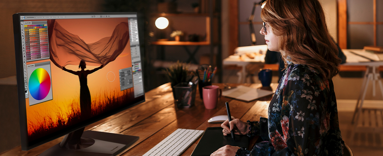 a woman sits at a desk editing a photo with a pen tablet